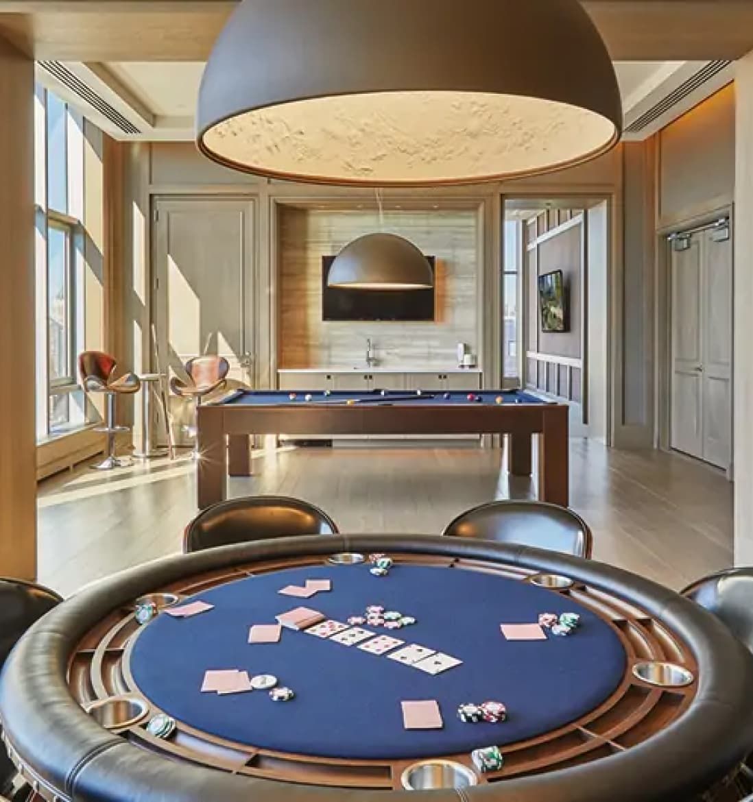 A poker table set in a EOS daylight-filled club room featuring a pool table, creating a lively atmosphere for games and socializing.