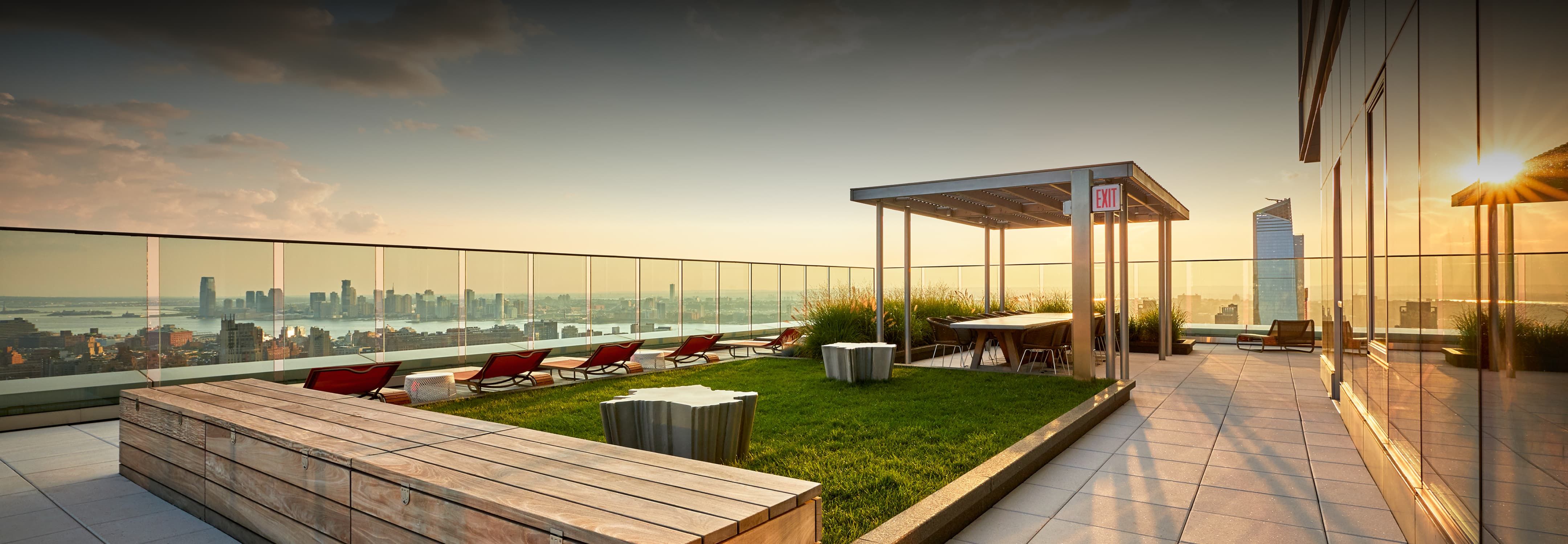 Rooftop deck with a lush grassy area and comfortable benches, ideal for leisure and social gatherings in an urban setting.