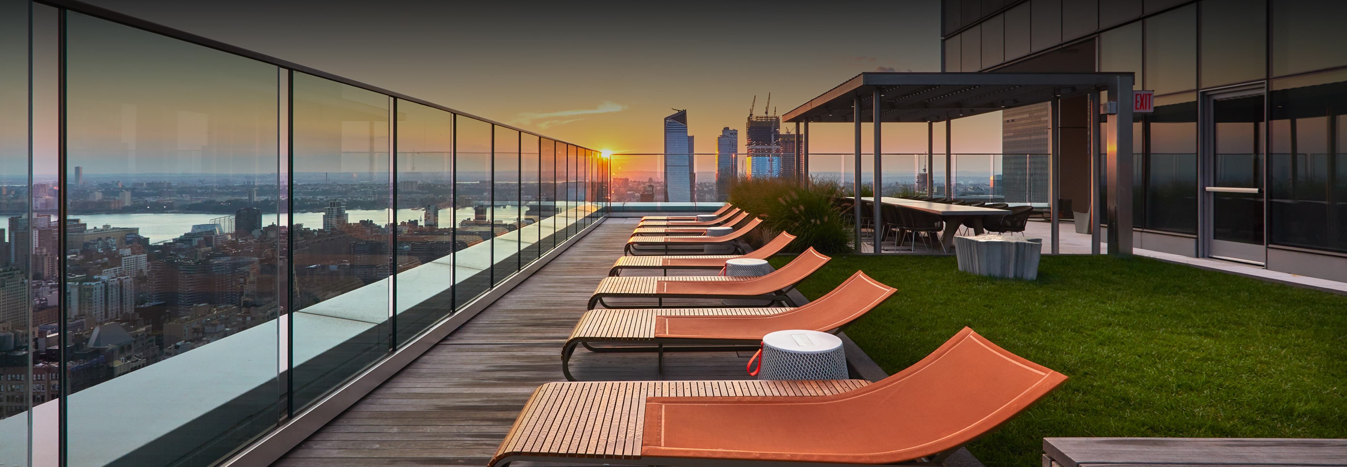 A panoramic view of the New York City skyline from a rooftop, showcasing iconic skyscrapers against a clear blue sky.