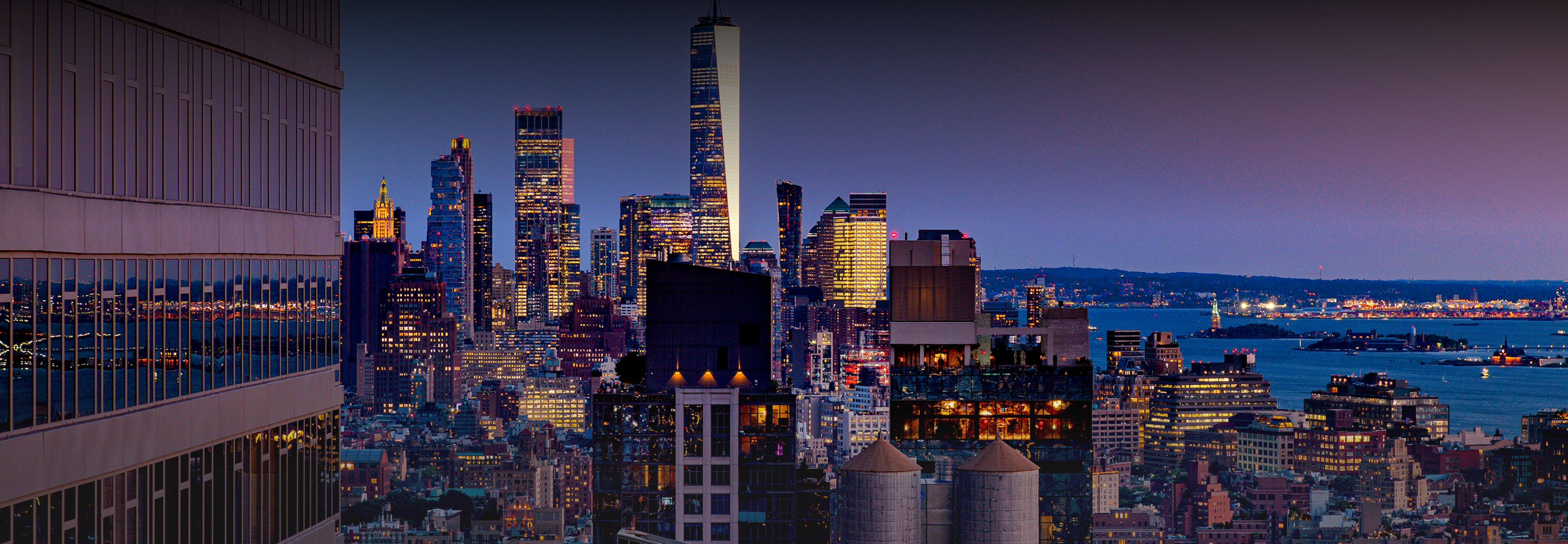 A panoramic view of a city skyline at New York, with buildings silhouetted against a colorful twilight sky.