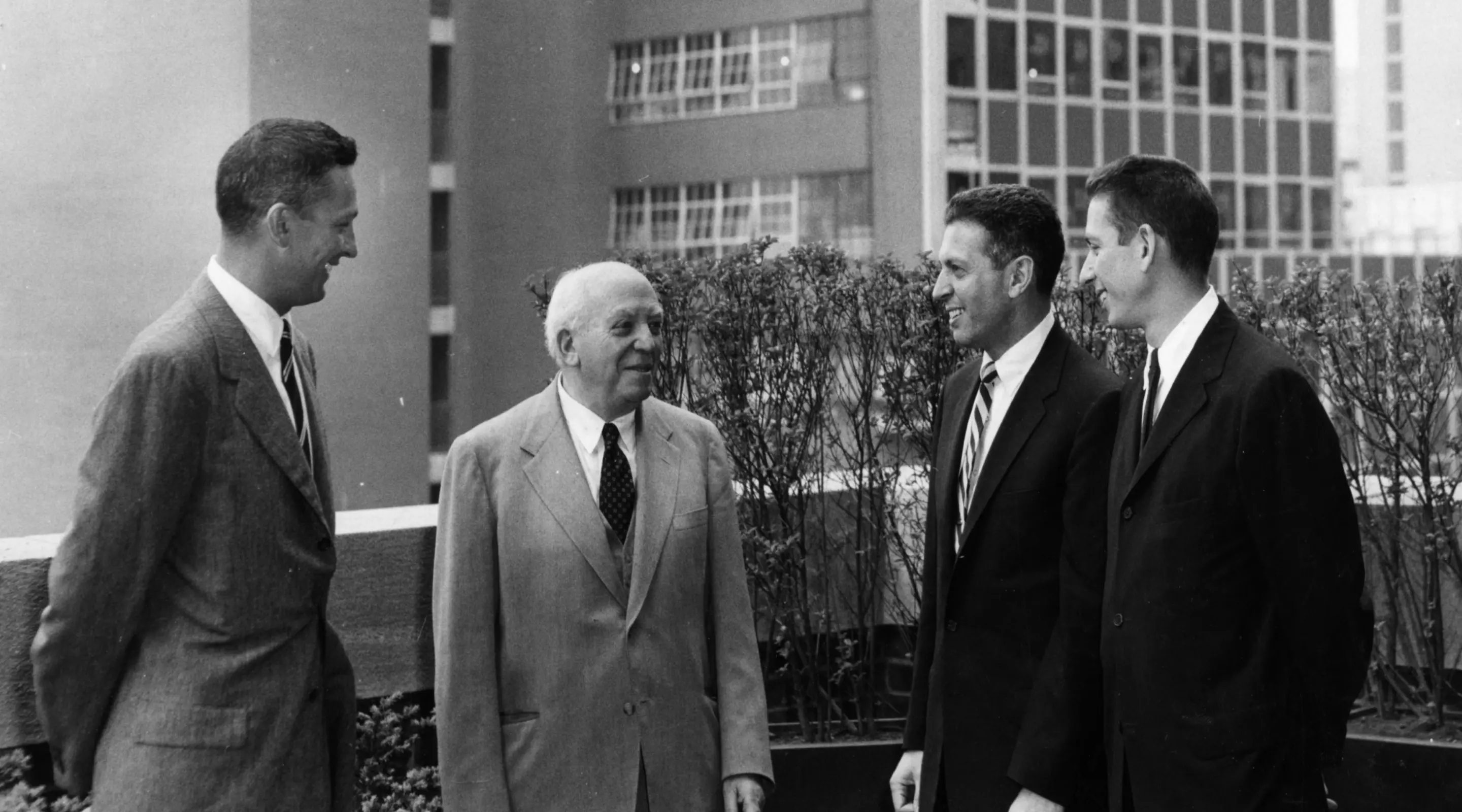 Four men in suits pose confidently in front of a modern building, showcasing professionalism and camaraderie.